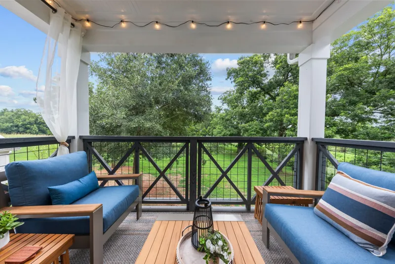 Covered upstairs patio with blue cushioned seating and string lights, overlooking trees and lawn